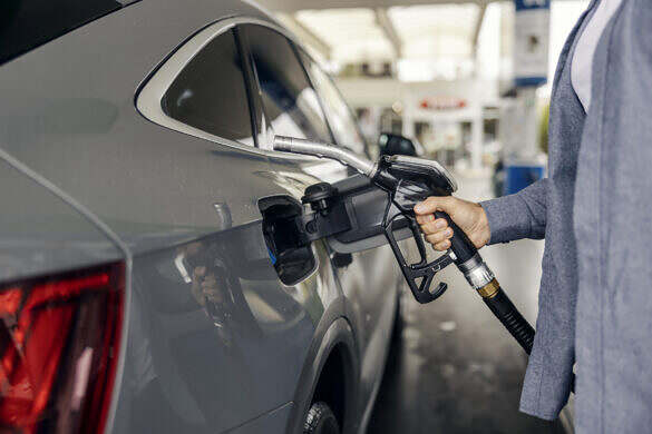 Person's hand holding a fuel nozzle, inserting it into a car's fuel tank at a gas station, highlighting daily commute, energy consumption, and increasing fuel prices