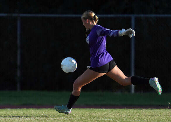 Female Soccer Goalie in uniform with cleats and gloves on a natural grass field in front of the goal/