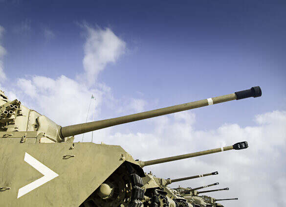 A line of tanks, gun barrels ready to attack.  Vibrant blue sky in the background with room for copy space.