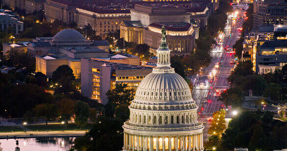High angle helicopter shot of the Capitol Building in Washington, D.C. at twilight on a clear evening in Fall, with the Federal Trade Commission Headquarters on Pennsylvania Avenue beyond.